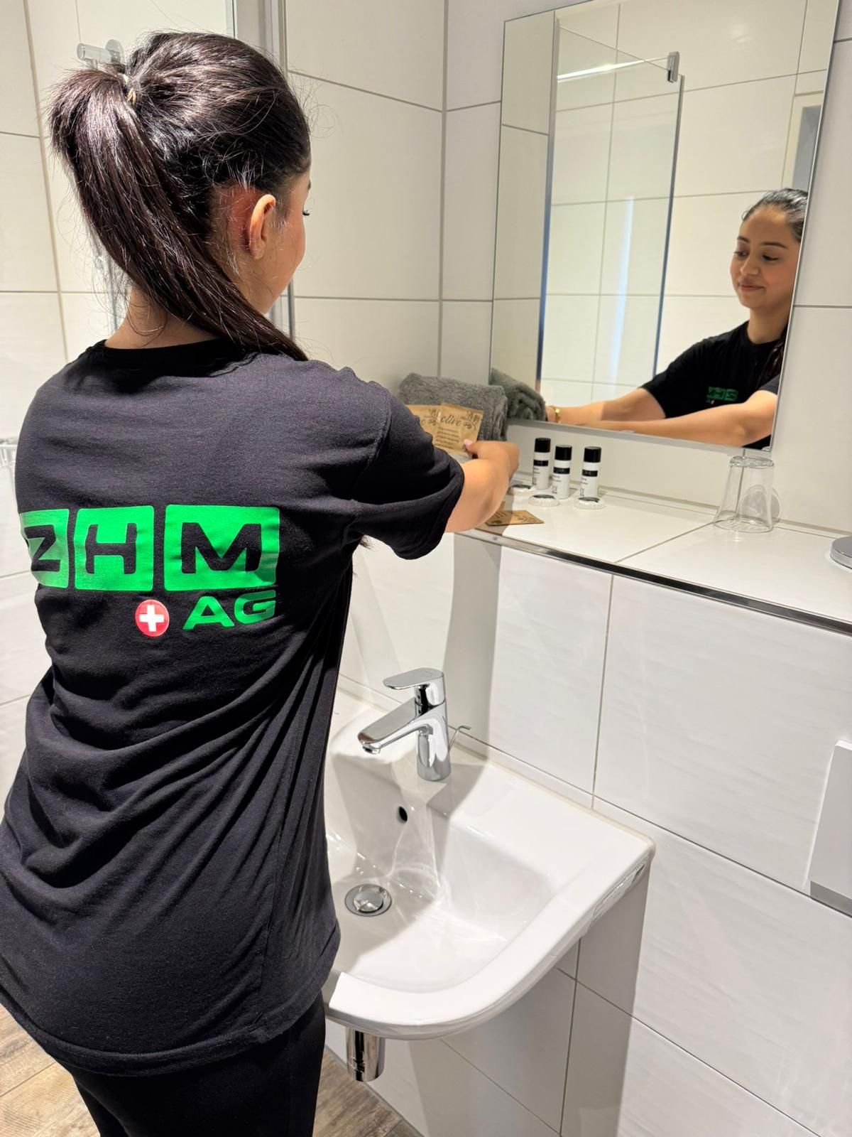 ZHM Mitarbeiterin reinigt ein Lavabo mit Spiegel